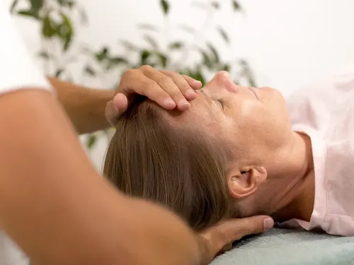Craniosacrale Energiearbeit: Hände halten den Kopf einer bekleidet auf einer Liege ruhenden Person.